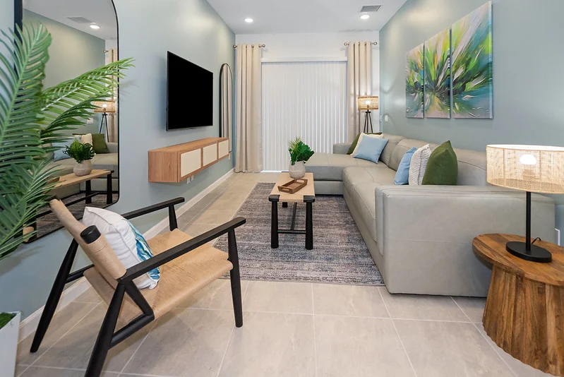 Bright living room with a light sectional sofa, wood accent chairs and tropical leaf art in the Paradiso Grande Ebb Tide Lane vacation rental furnished by Furniture Packages USA