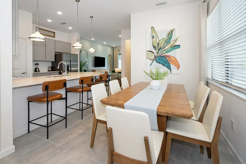 Open kitchen with leather counter stools and a wood dining table with white chairs in the Paradiso Grande Ebb Tide Lane home